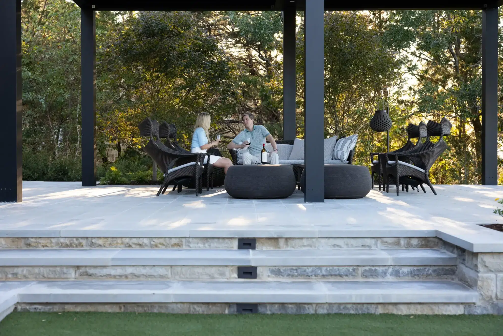 Couple relaxing under painted steel pergola on limestone patio at Deer Valley Cedar Creek Lake outdoor living space designed by Landvisions