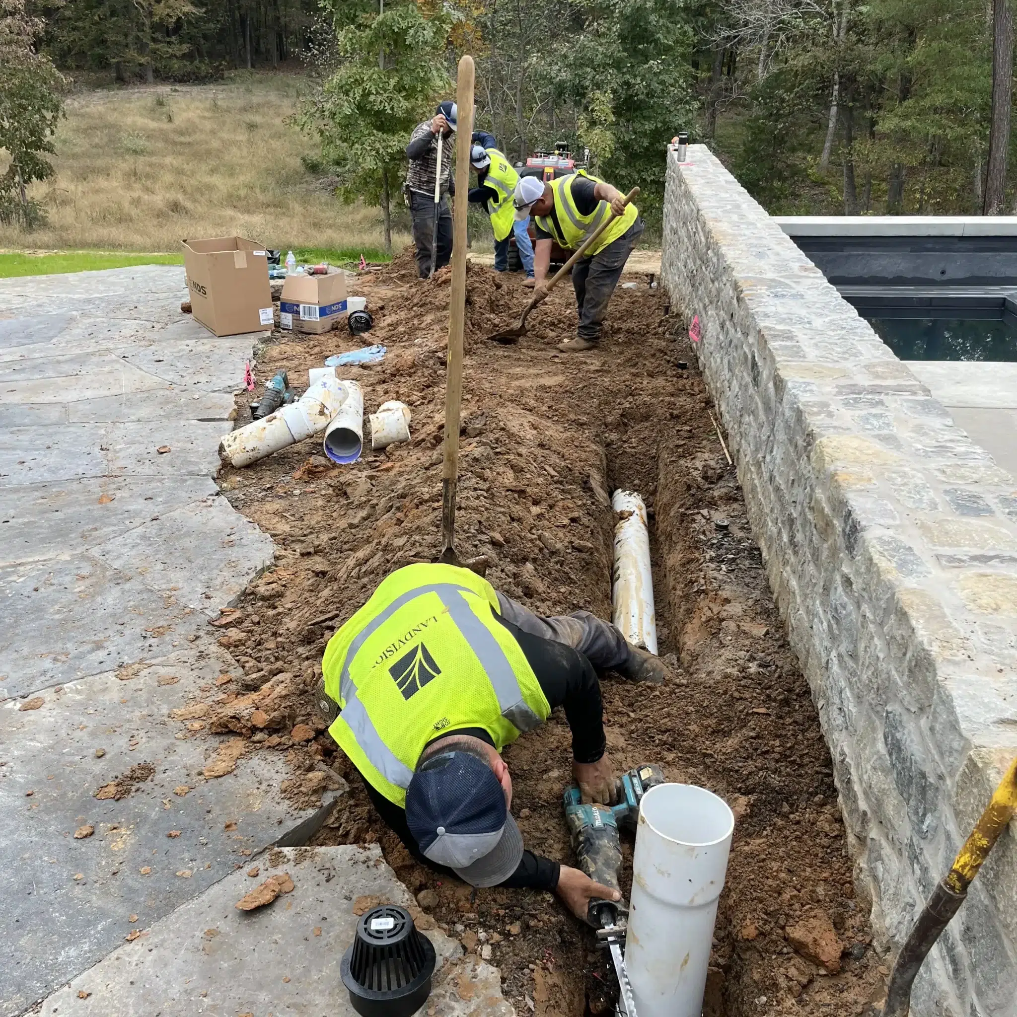 Landvisions crew installing irrigation and drainage system alongside stone retaining wall at East Texas landscape project