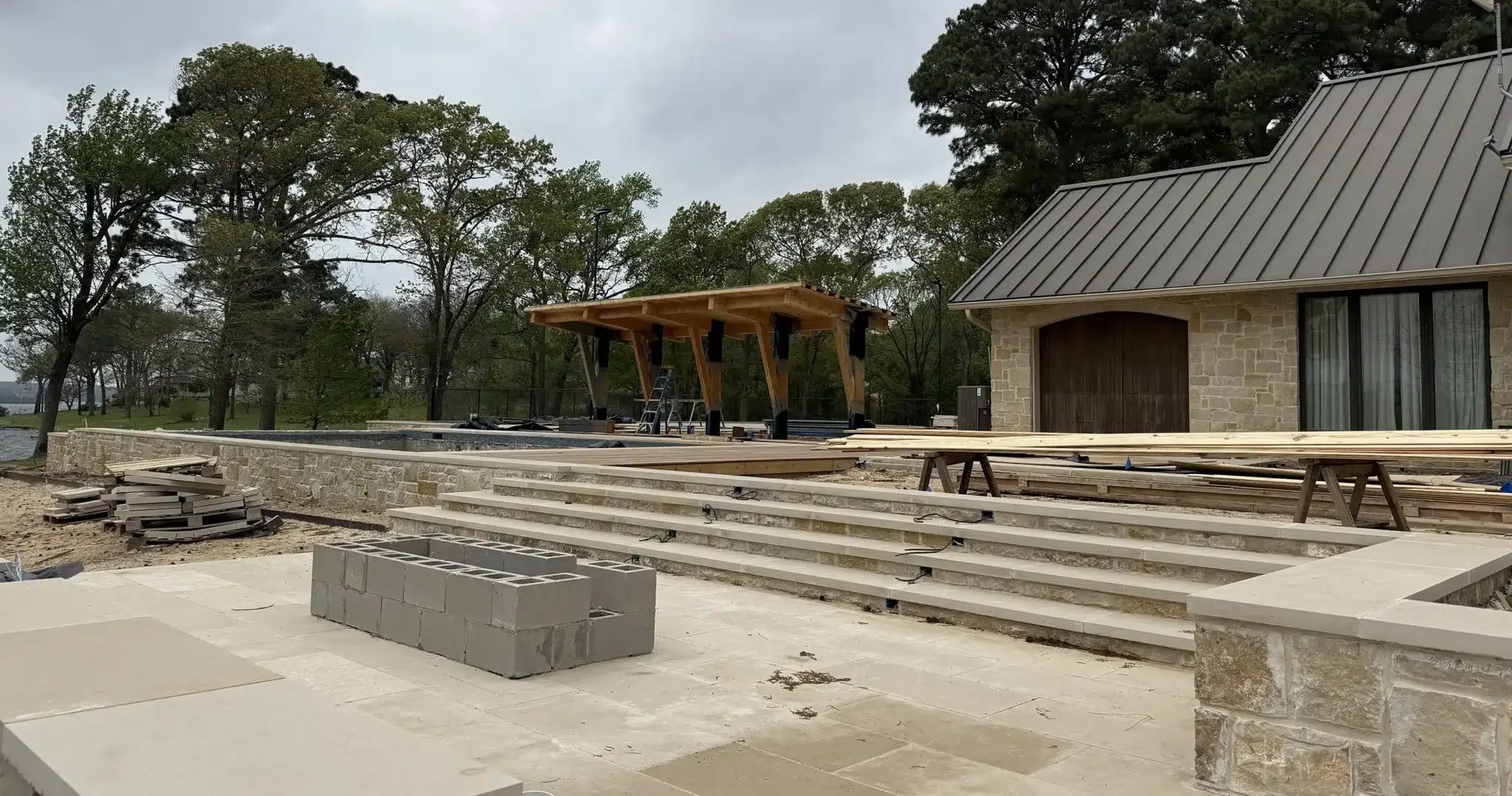 Landvisions construction in progress at East Texas lake property showing limestone terrace steps, pool shell, and timber pergola framing